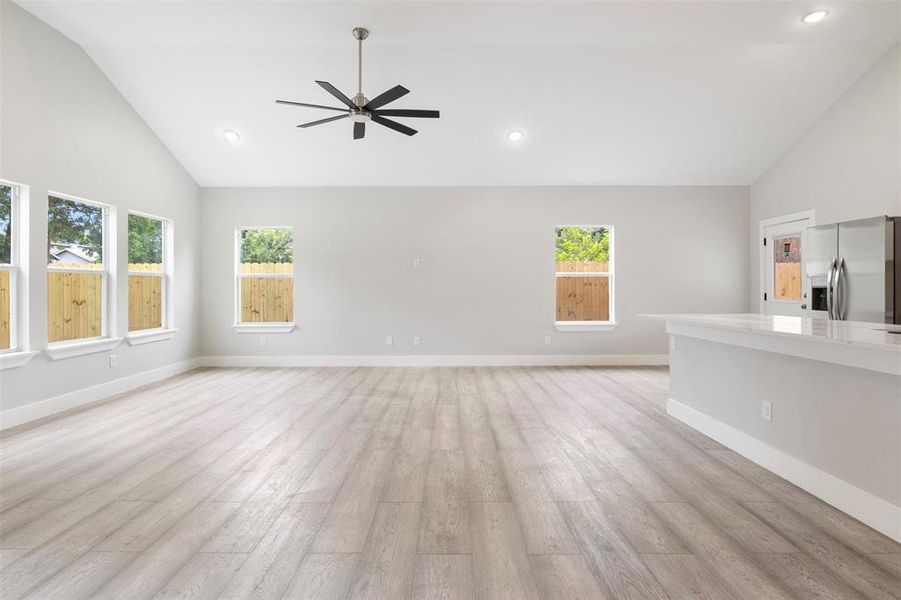 Unfurnished living room with a healthy amount of sunlight, high vaulted ceiling, light wood-type flooring, and ceiling fan