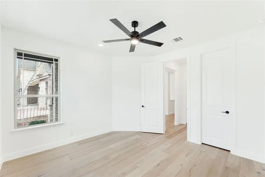 Empty bedroom with light hardwood floors, black ceiling fan, and two white doors