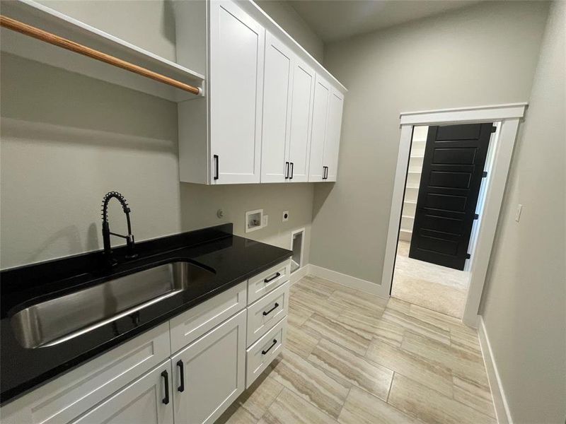 Laundry area featuring white shaker-style cabinetry, a deep stainless steel utility sink with a black industrial-style faucet, dark countertops, and wood-look tile flooring