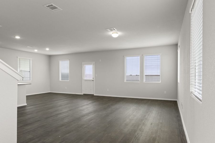 Image of a living room with dark vinyl flooring and light grey walls with windows and a white back door