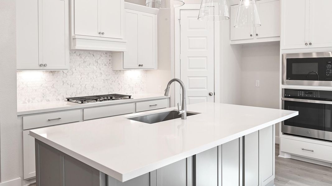 Kitchen with stainless steel appliances, tasteful backsplash, a kitchen island with sink, hanging light fixtures, and white cabinetry Kitchen with stainless steel appliances, tasteful backsplash, a kitchen island with sink, hanging light fixtures, and white cabinetry