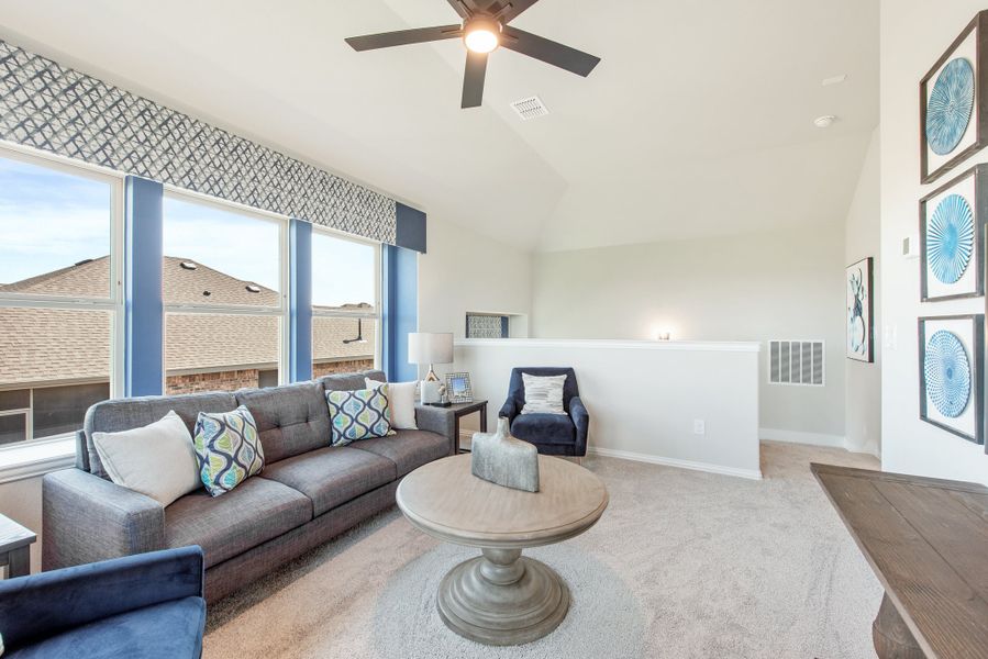 Upstairs living area with vaulted ceiling, ceiling fan, gray sofa, and large windows with blue curtains
