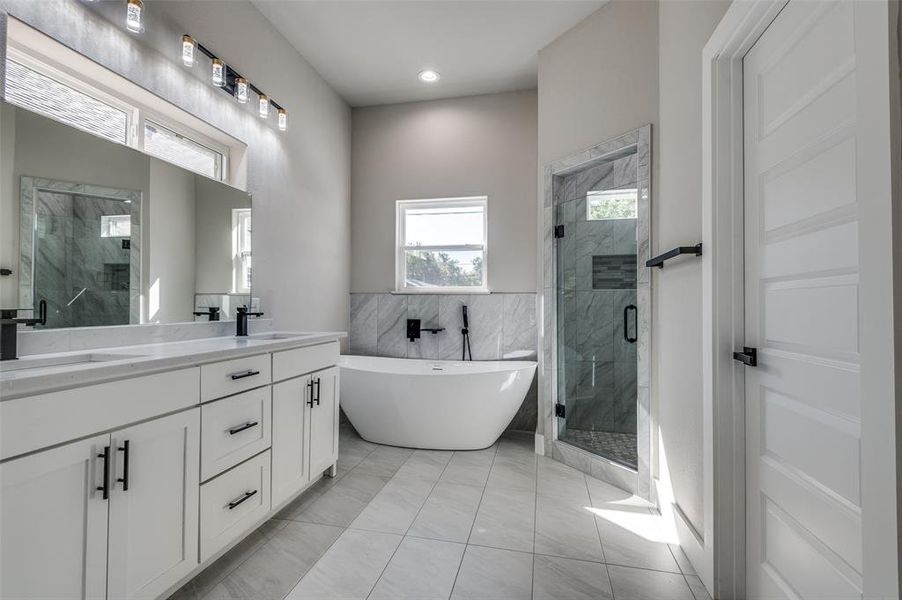 Full bathroom with a marble finish shower, a soaking tub, double vanity, and tile walls Full bathroom with a marble finish shower, a soaking tub, double vanity, and tile walls