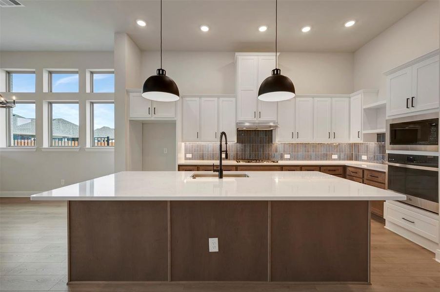 Kitchen with decorative backsplash, stainless steel appliances, dual tone cabinetry, light wood-style floors, and a kitchen island with sink