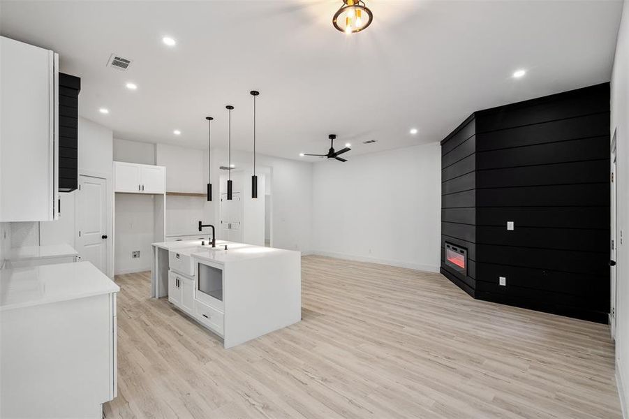 Kitchen with hanging light fixtures, light hardwood / wood-style flooring, white cabinetry, ceiling fan, and a center island with sink