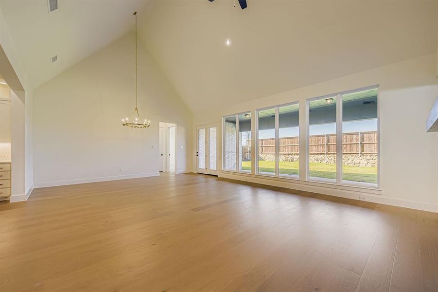 Unfurnished living room with high vaulted ceiling, a chandelier, and light wood-style flooring