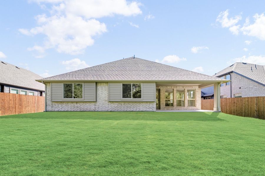 Rear exterior of single-story brick home with covered patio, large green backyard, and wood privacy fence