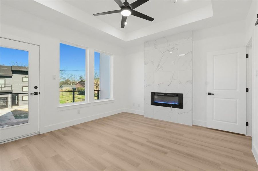 Unfurnished living room featuring a ceiling fan, a high end fireplace, light wood-style flooring, and a tray ceiling
