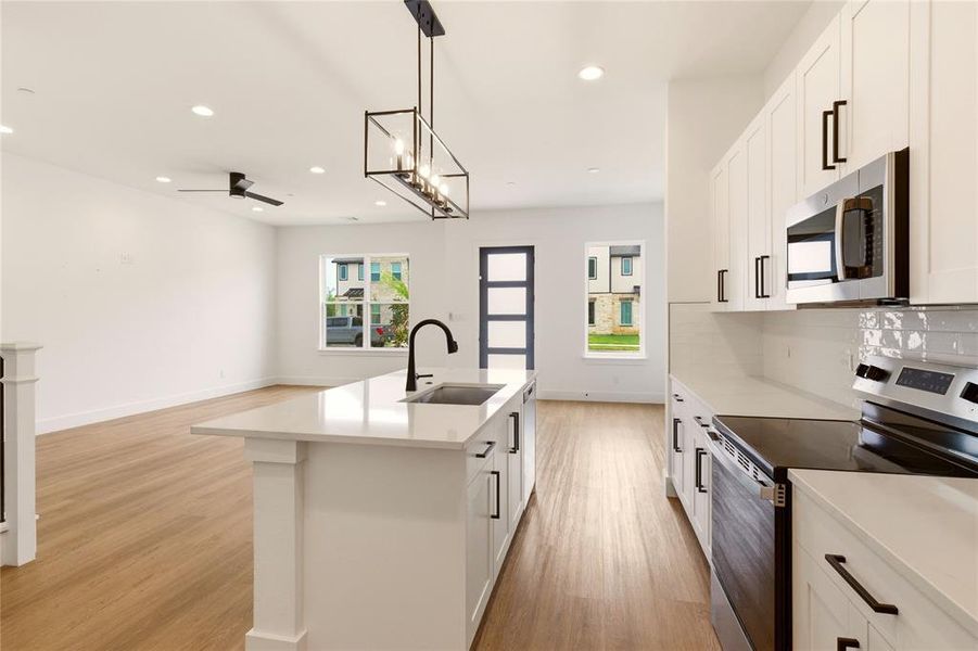 Kitchen featuring stainless steel appliances, a kitchen island with sink, light wood-style flooring, white cabinetry, and ceiling fan