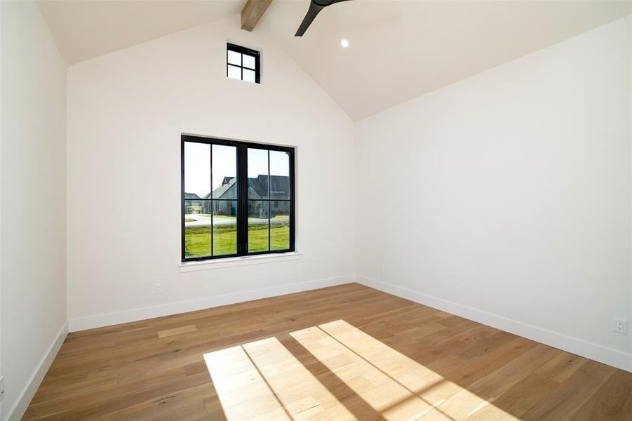 Empty room with lofted ceiling with beams, light hardwood / wood-style floors, and ceiling fan