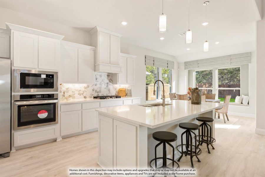 Open kitchen with white cabinets, large island with bar stools, stainless steel appliances, and light wood floors