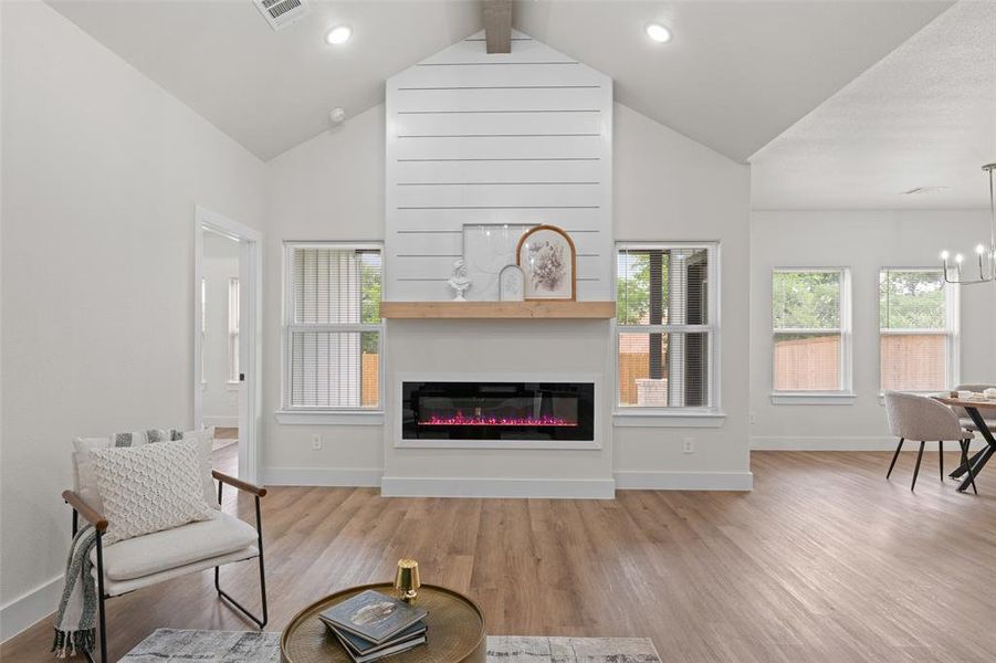 Living area with wood finished floors, baseboards, a glass covered fireplace, a chandelier, and high vaulted ceiling Living area with wood finished floors, baseboards, a glass covered fireplace, a chandelier, and high vaulted ceiling