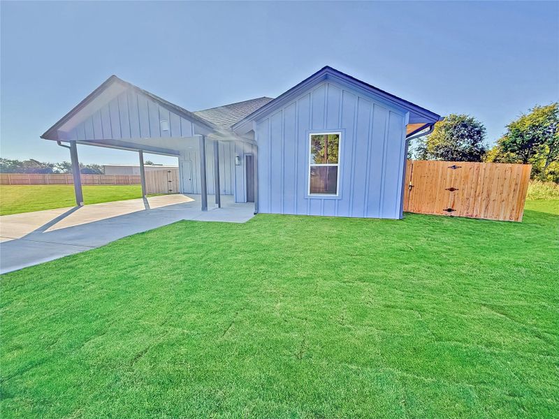View of front of house with board and batten siding, an attached carport, and concrete driveway. This image enhanced by AI to showcase the newly installed carpet grass. Please note the carpet grass covers only a portion of the yard, not the entire area.