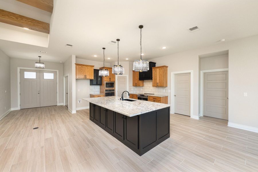 Kitchen featuring tasteful backsplash, brown cabinets, light stone countertops, a center island with sink, and wood finish floors Kitchen featuring tasteful backsplash, brown cabinets, light stone countertops, a center island with sink, and wood finish floors