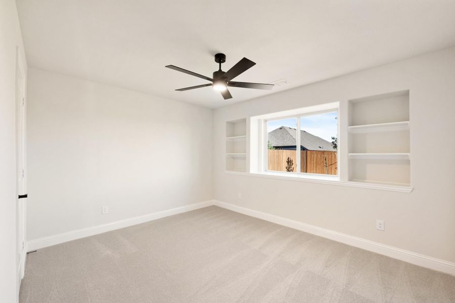 Empty bedroom with carpet, ceiling fan, window, and built-in wall shelves