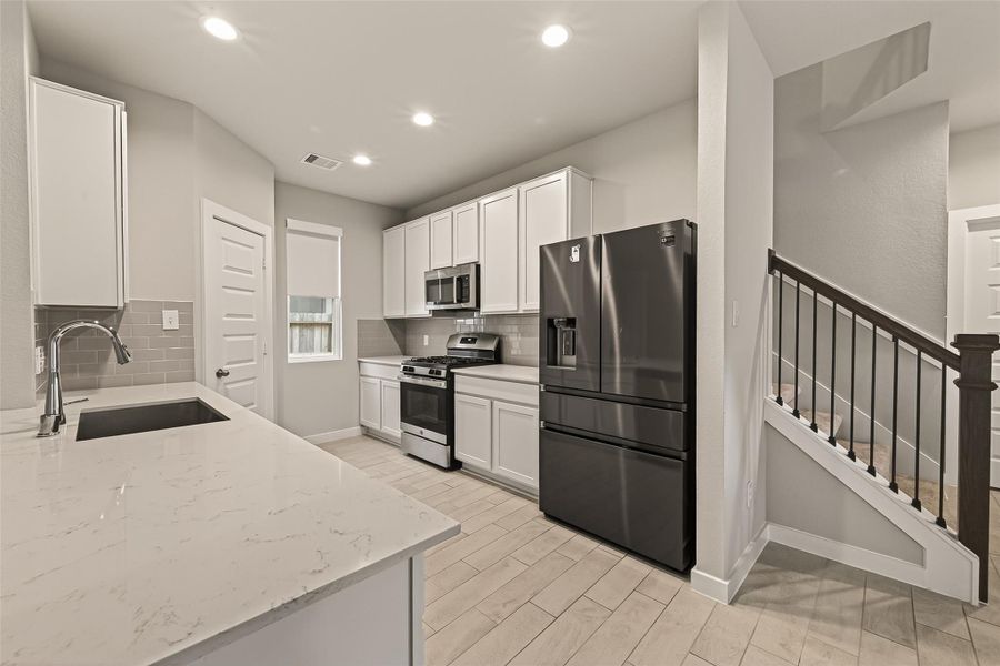 This view shows the full kitchen layout, with a staircase at the back providing access to the upper level.