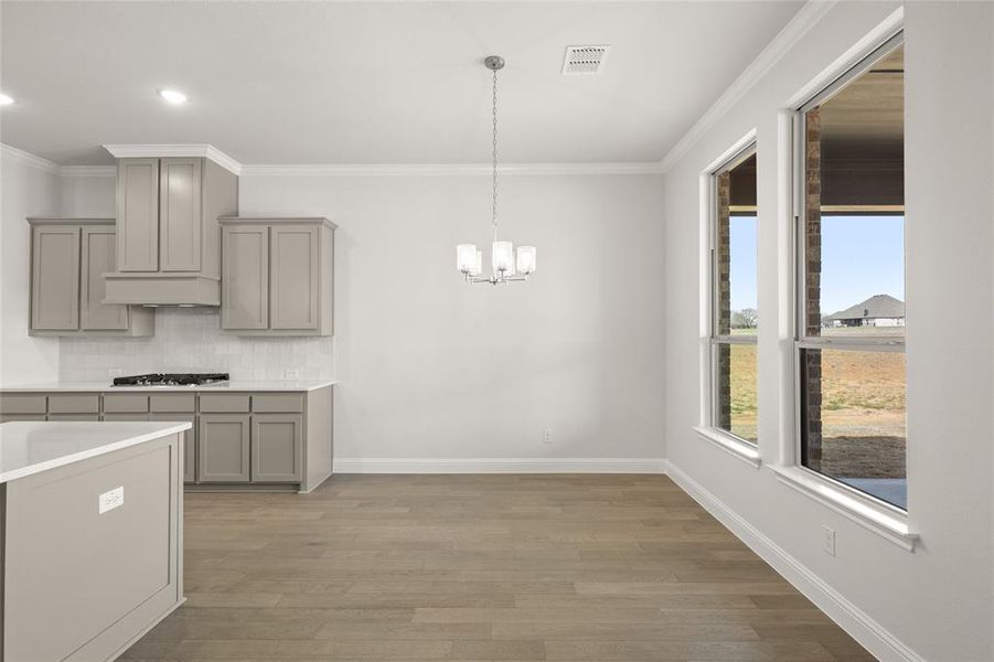 Kitchen featuring gray cabinets, stainless steel gas cooktop, a chandelier, crown molding, and tasteful backsplash Kitchen featuring gray cabinets, stainless steel gas cooktop, a chandelier, crown molding, and tasteful backsplash