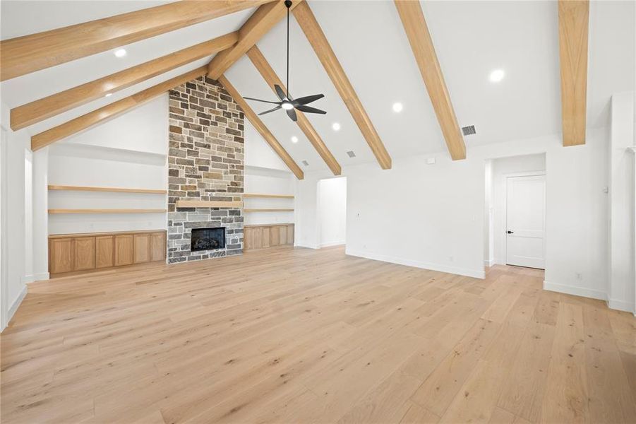 Unfurnished living room with beam ceiling, light wood-style flooring, high vaulted ceiling, a fireplace, and recessed lighting