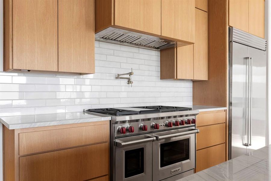 Kitchen featuring high end appliances, backsplash, light stone counters, and modern cabinets Kitchen featuring high end appliances, backsplash, light stone counters, and modern cabinets