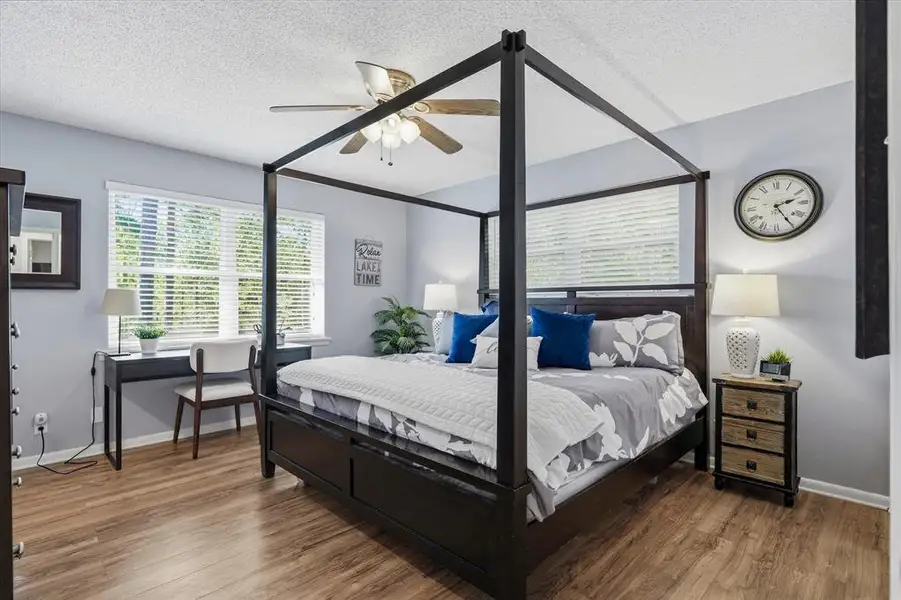 Spacious room featuring wood-finish flooring, two large windows with blinds, and a ceiling fan