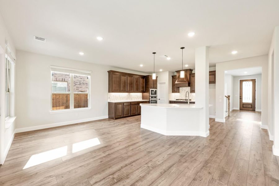Open-concept kitchen with dark wood cabinets, white island, and light hardwood floors