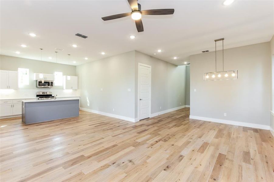 Kitchen with white cabinets, appliances with stainless steel finishes, pendant lighting, and light hardwood / wood-style floors