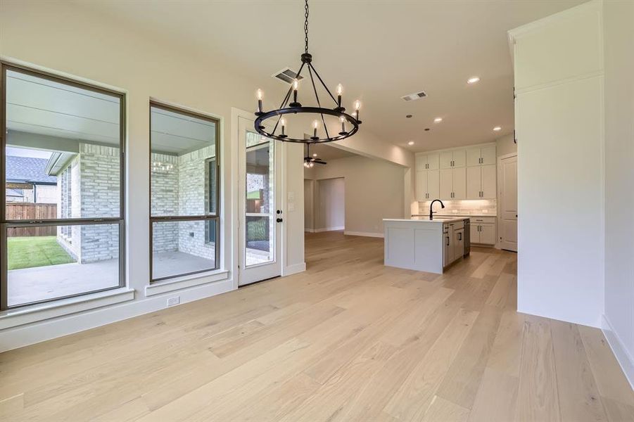 Kitchen with a chandelier, light wood-style floors, a kitchen island with sink, white cabinets, and light countertops Kitchen with a chandelier, light wood-style floors, a kitchen island with sink, white cabinets, and light countertops