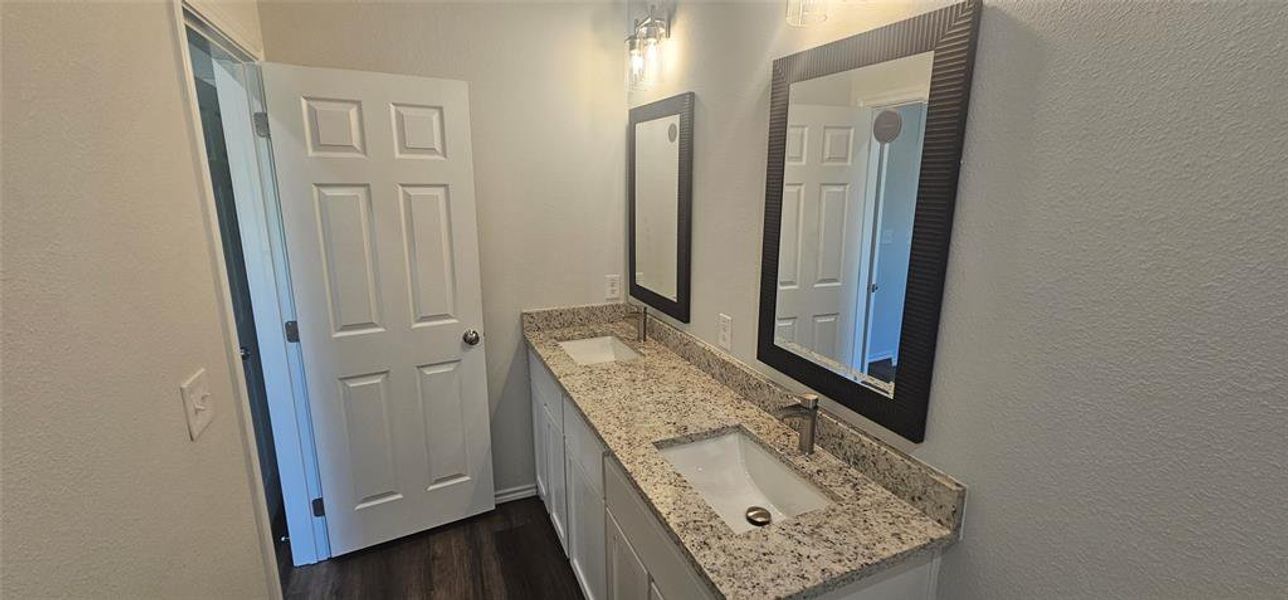 Full bath featuring a textured wall, double vanity, and dark wood-style floors