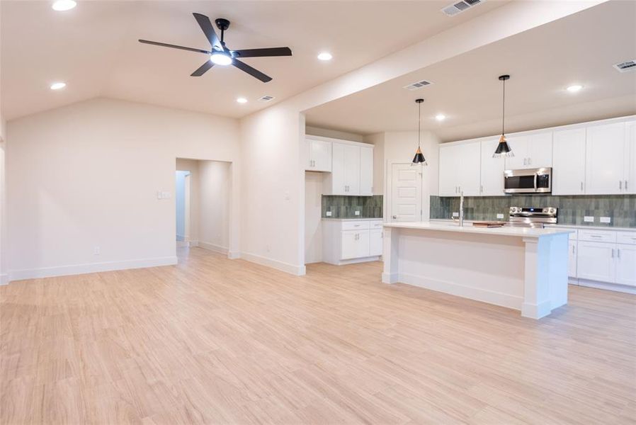 Kitchen featuring decorative backsplash, light wood-style floors, white cabinets, a center island with sink, and hanging light fixtures