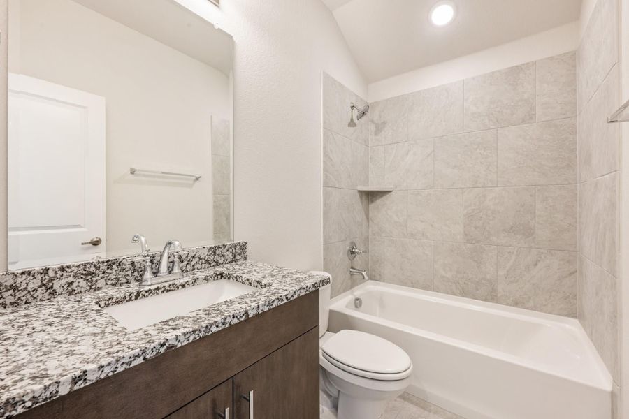 Bathroom with granite vanity, dark wood cabinets, and tiled tub-shower combo