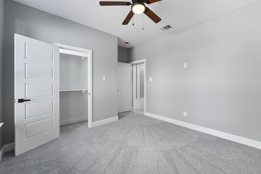 Unfurnished bedroom featuring light colored carpet, a spacious closet, and a ceiling fan Unfurnished bedroom featuring light colored carpet, a spacious closet, and a ceiling fan