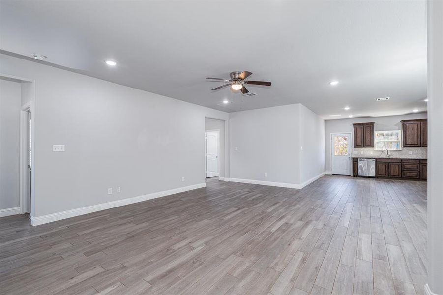 Unfurnished living room featuring a ceiling fan, light wood-type flooring, a sink, and baseboards