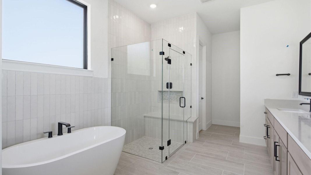 Luxurious primary bathroom with dual vanities, a soaking tub, and separate glass-enclosed walk in shower