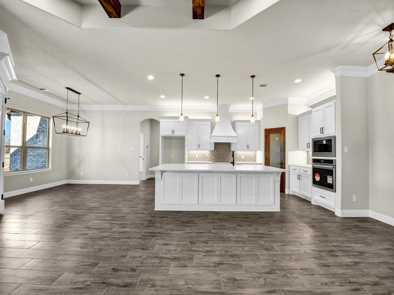 Kitchen featuring built in microwave, stainless steel oven, decorative light fixtures, custom range hood, and a kitchen island with sink