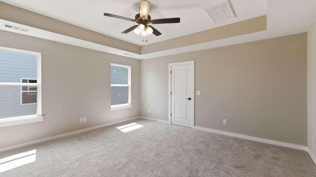 Primary suite with tray ceiling, ceiling fan, and carpet Primary suite with tray ceiling, ceiling fan, and carpet