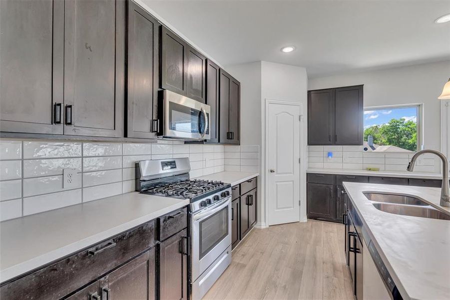 Kitchen with range with gas stovetop, tasteful backsplash, sink, dark brown cabinetry, and light wood-type flooring