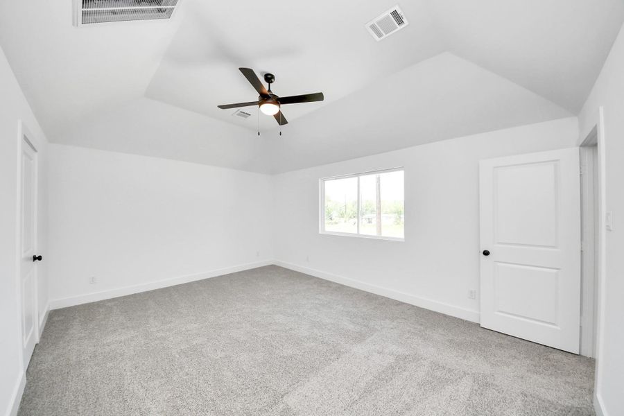 Primary Bedroom – Spacious and bright primary suite with plush carpeting, vaulted ceiling, modern ceiling fan, large windows, and plenty of natural light.
