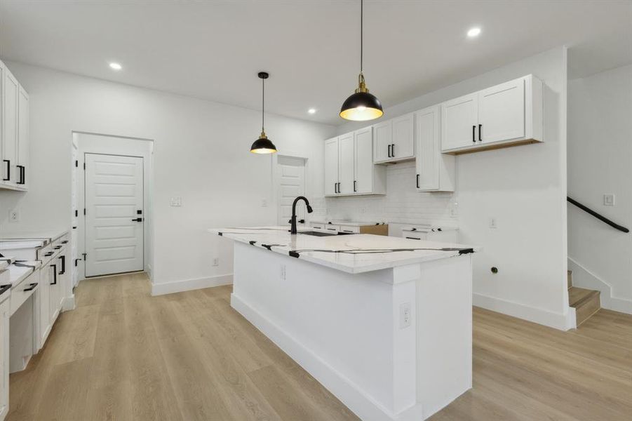 Kitchen with sink, an island with sink, white cabinets, and light hardwood / wood-style floors