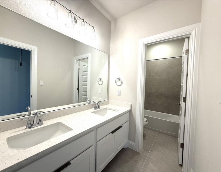 Full bath with double vanity, light tile patterned flooring, and bathing tub / shower combination