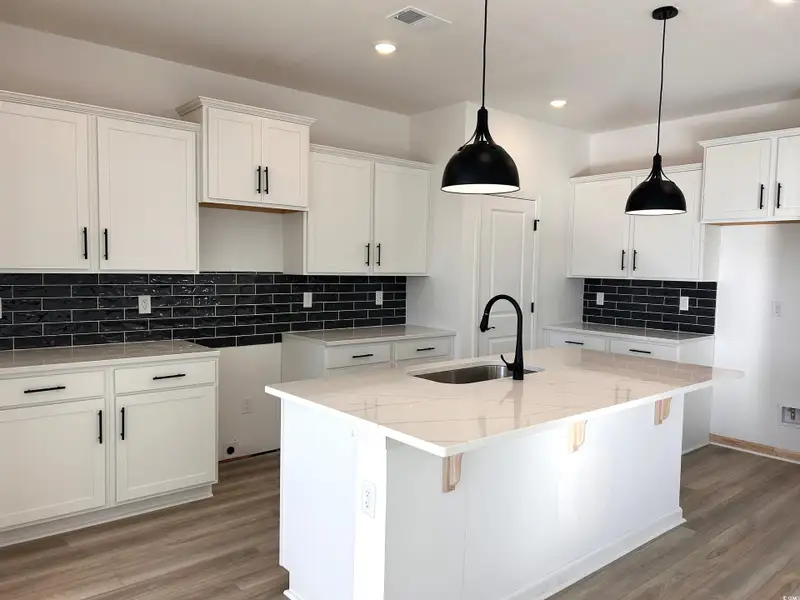 Kitchen with white cabinetry, a kitchen breakfast bar, decorative backsplash, light stone countertops, and decorative light fixtures