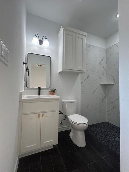 Bathroom featuring toilet, tiled shower, and vanity