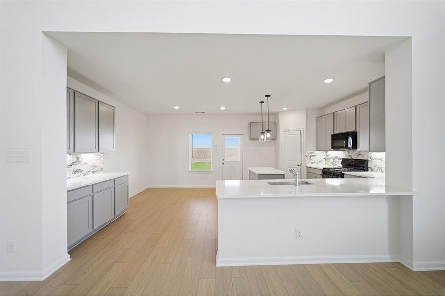 Kitchen with tasteful backsplash, gray cabinets, black appliances, light wood finished floors, and a peninsula