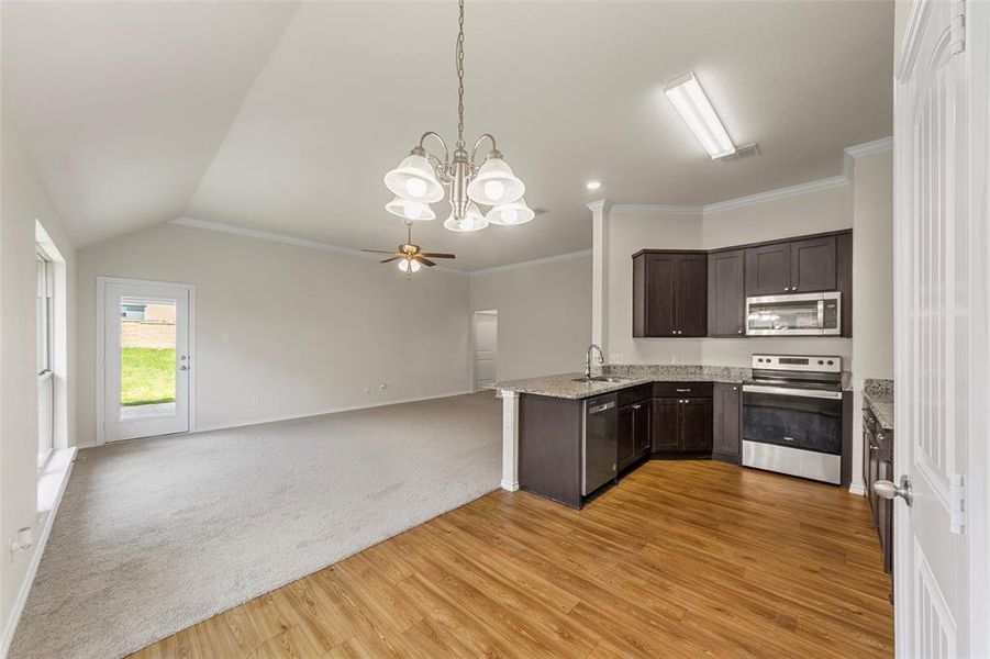 Kitchen featuring appliances with stainless steel finishes, dark brown cabinetry, light stone countertops, light wood-type flooring, and open floor plan Kitchen featuring appliances with stainless steel finishes, dark brown cabinetry, light stone countertops, light wood-type flooring, and open floor plan