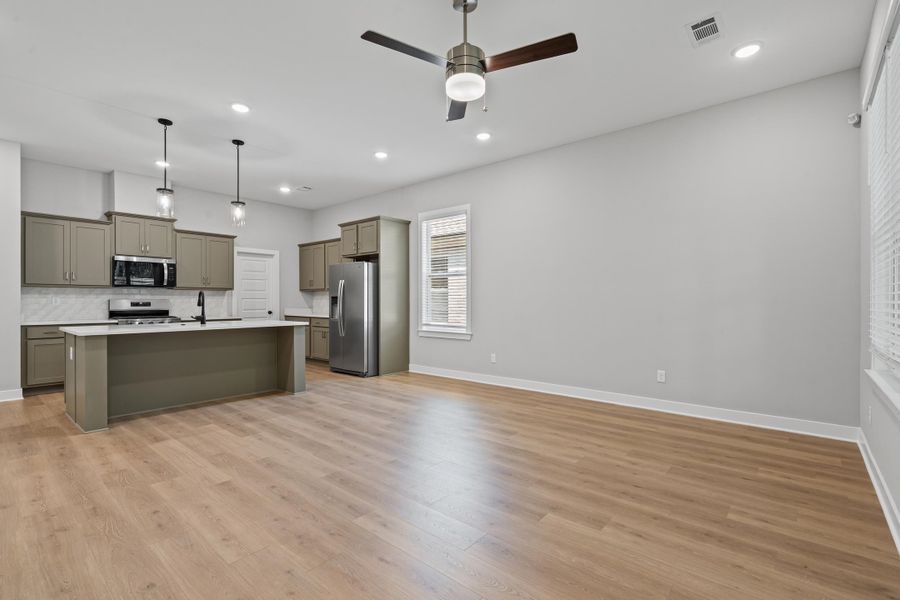 Kitchen featuring tasteful backsplash, decorative light fixtures, an island with sink, stainless steel appliances, and light wood-style floors