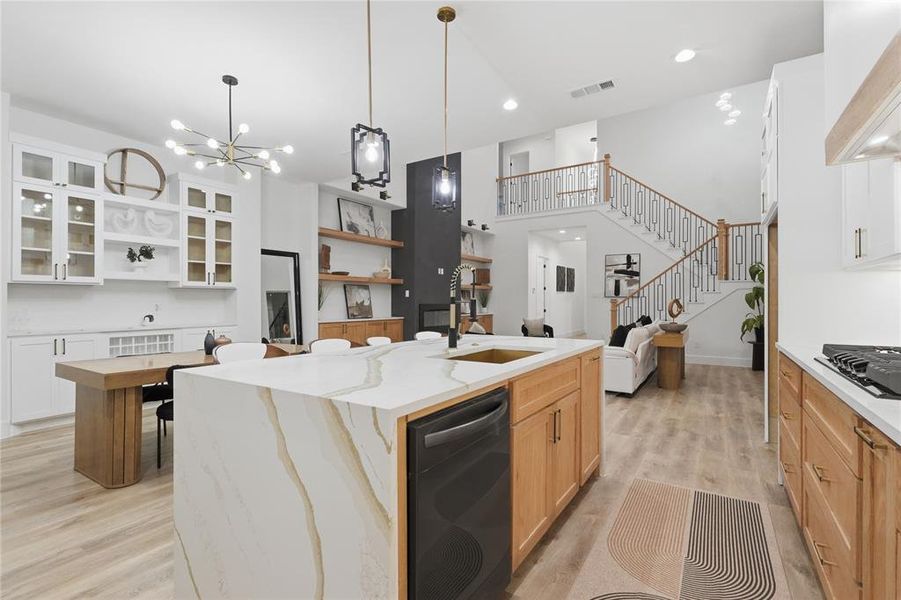Kitchen featuring a center island with sink, light stone countertops, black appliances, glass insert cabinets, and light wood-type flooring