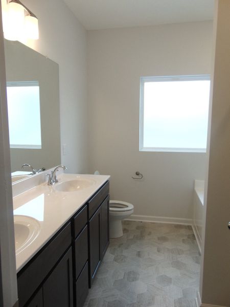 The primary bathroom comes with a two sink, soaking bath tub, shower, and an elongated toilet.