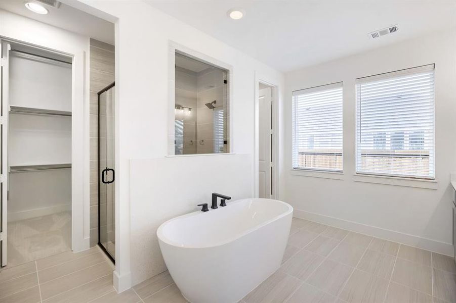 Freestanding bathtub with matte black fixtures, set against light tile flooring