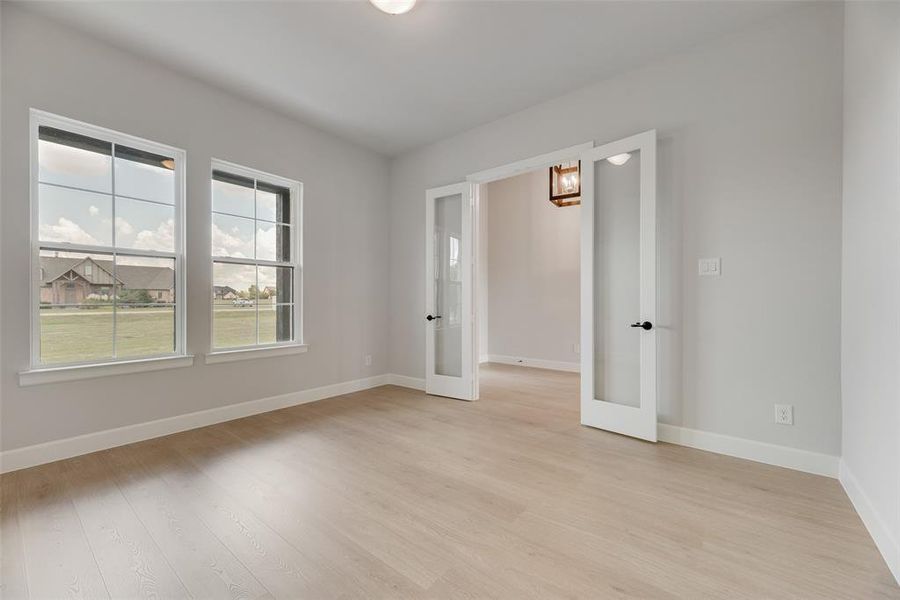 Empty room featuring french doors, light wood-type flooring, and a chandelier
