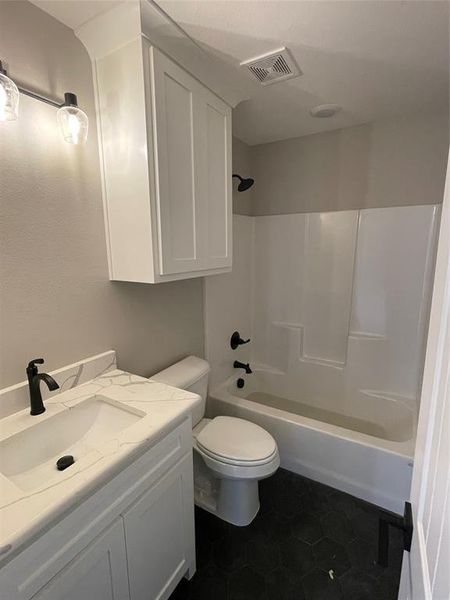 Full bathroom with washtub / shower combination, tile patterned floors, toilet, and vanity