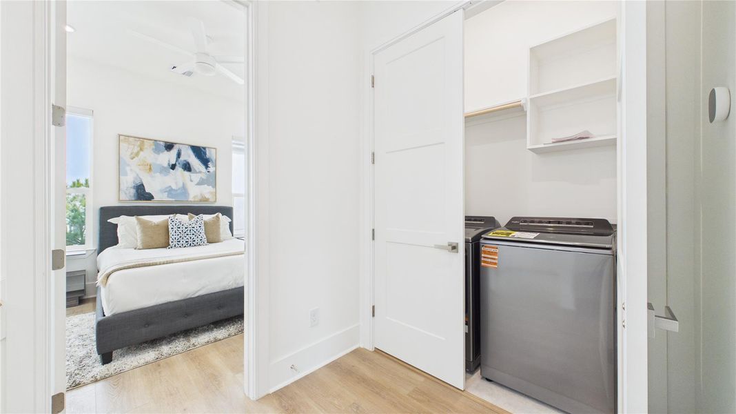 This photo shows a bright, modern bedroom with a comfortable bed, adjacent to a laundry area with a washer and dryer neatly tucked into a closet space.
